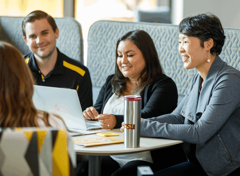 Three individuals sitting at table with laptop, discussing project