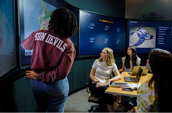 A small group watches a person present data on a large screen