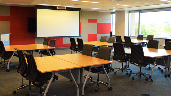 Another view of Global room set up as 6 squares of tables with chairs facing wall with monitors.