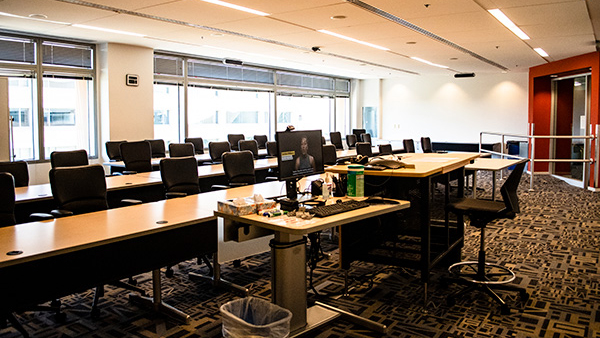 Exploration room set up classroom style with tales from front of room, also showing speaker podium and computer connections