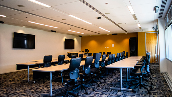 Exploration room set up classroom style with tales from back of room, also showing ceiling with speakers and AV equipment