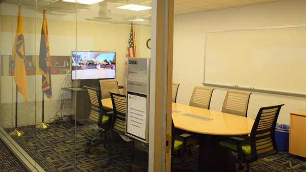 Acceleration boardroom looking through glass wall from hallway with conference table, chairs and computer monitor.