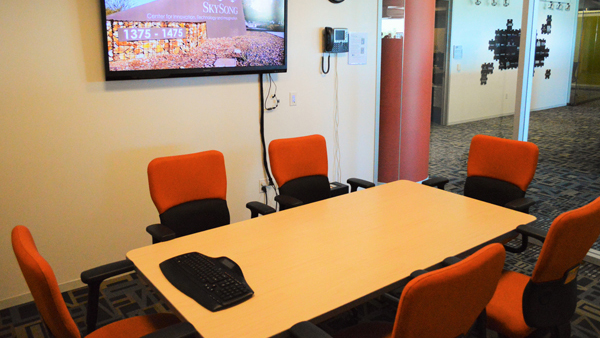Collaboration room with computer screen on wall, and table and chairs.