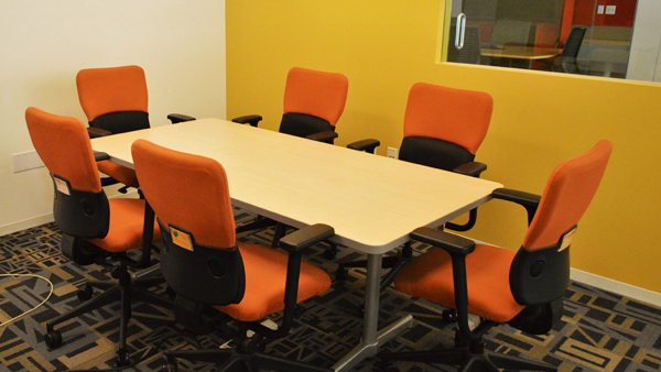 Confluence room table and chairs showing screen on the wall.