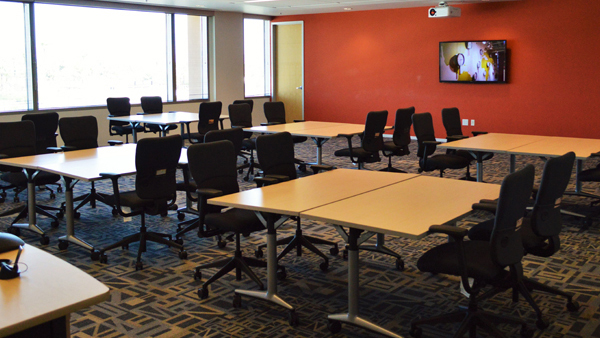 Ingenuity room showing tables, chairs, monitor on wall and windows.